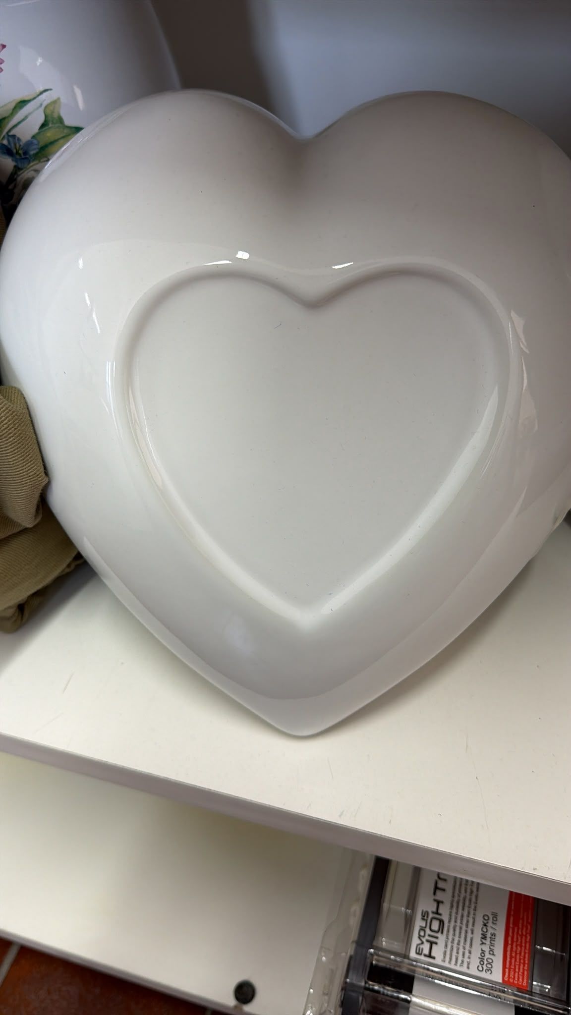 Oggetto decorativo bianco a forma di cuore su una mensola, con un motivo a cuore incassato.
