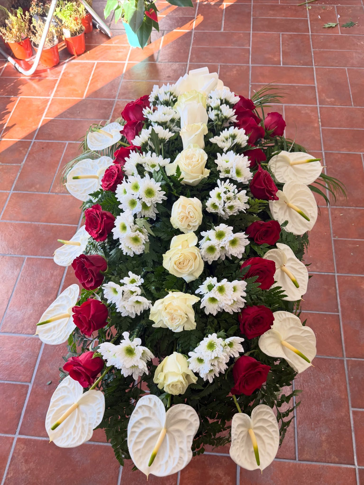 Ghirlanda di fiori bianchi e rossi disposta su piastrelle di terracotta, con rose e gigli che circondano fiori bianchi