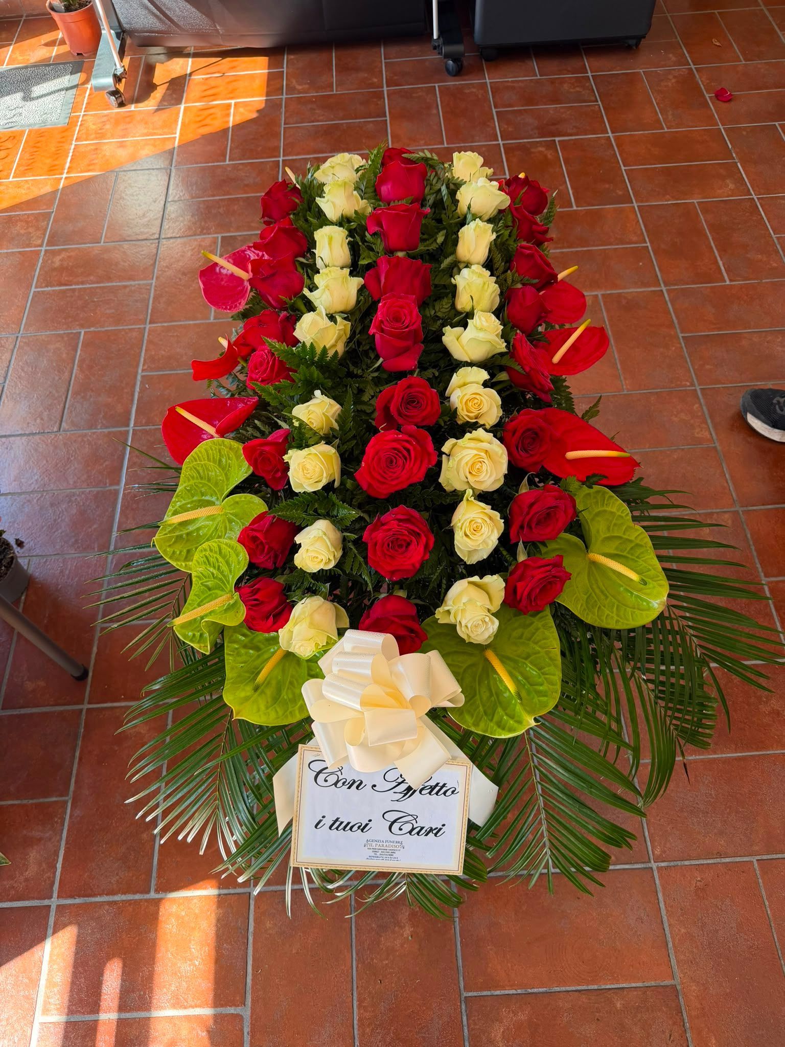 Ghirlanda floreale variopinta con fiori rossi, bianchi e gialli e un nastro bianco su un pavimento piastrellato