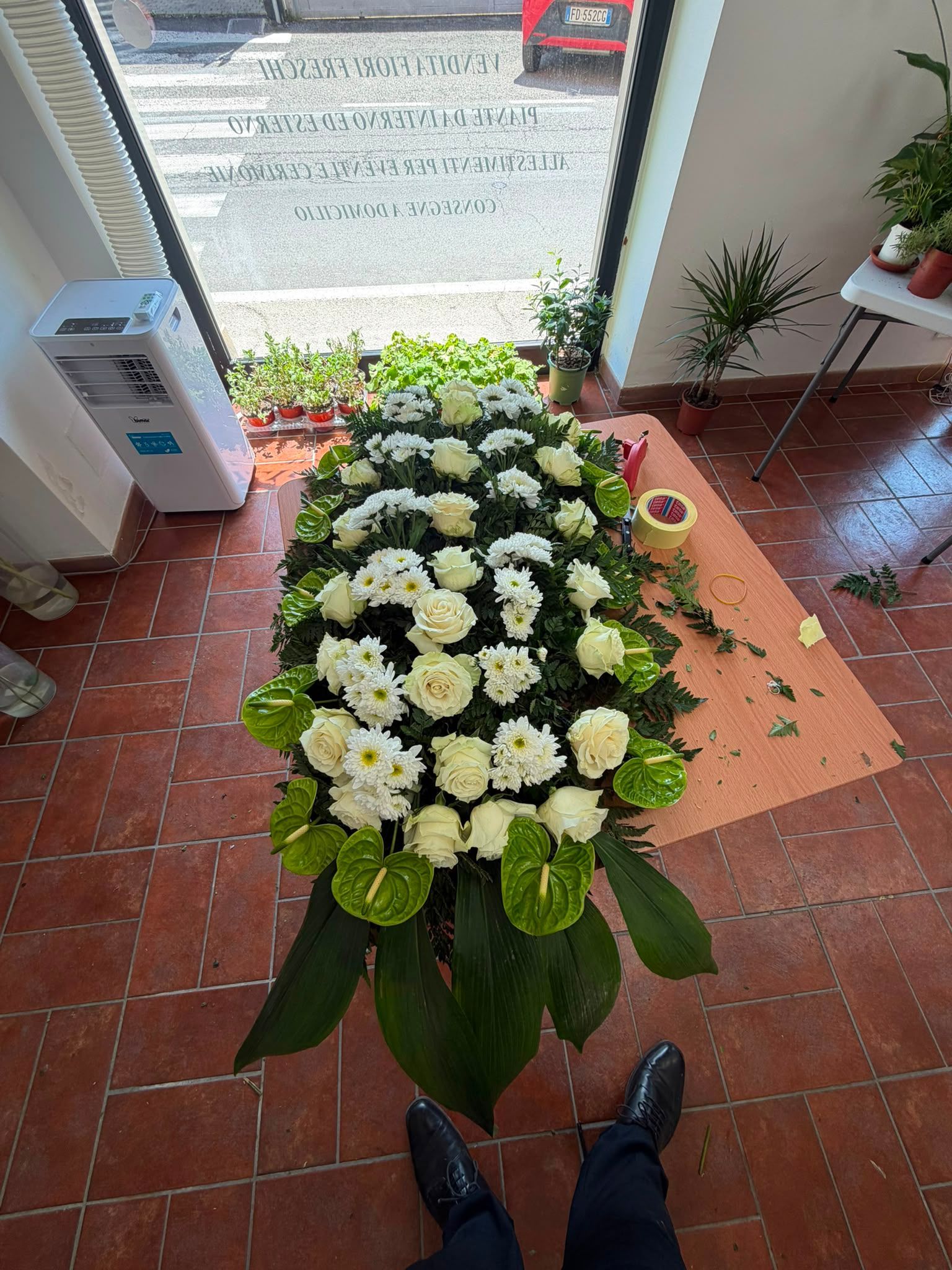 Composizione floreale con fiori bianchi e foglie verdi su un pavimento in mattoni vicino a una porta.
