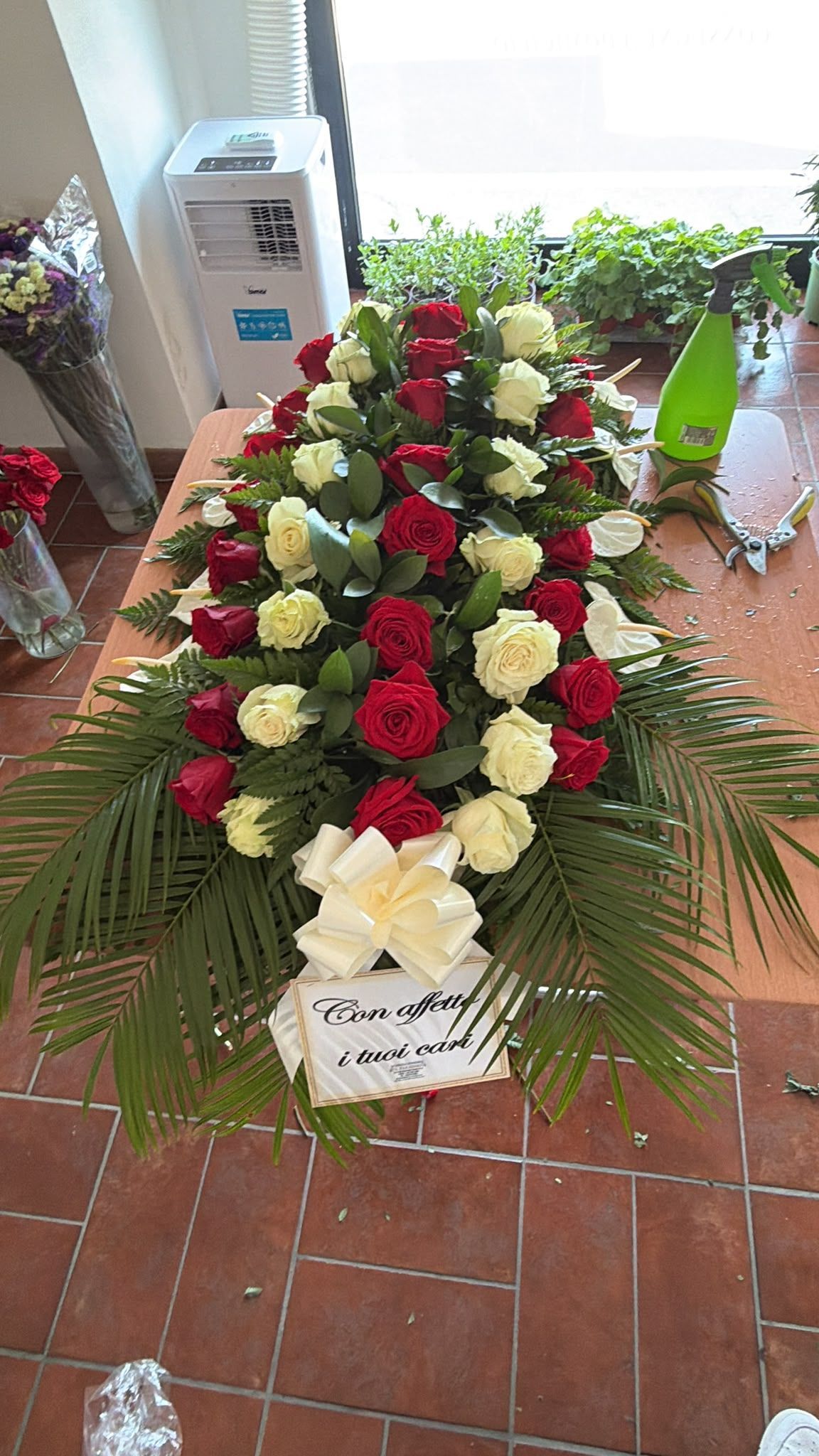 Grande corona floreale di rose rosse e bianche con foglie di palma su un pavimento piastrellato al chiuso
