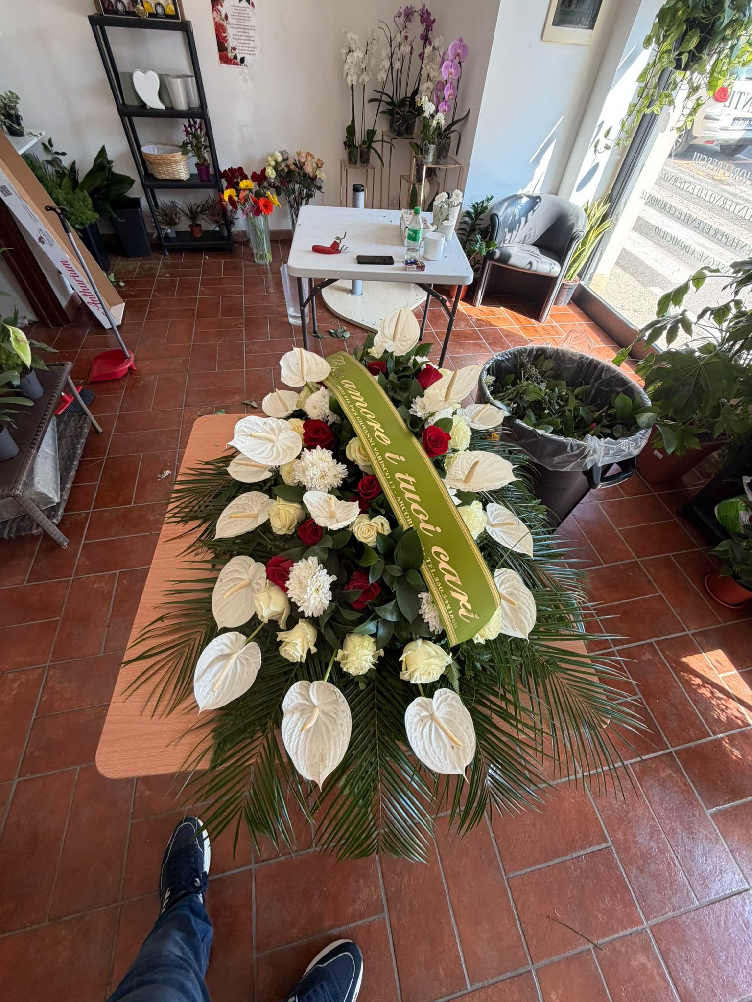 Ghirlanda di fiori bianchi e rossi su un pavimento piastrellato, in un contesto commemorativo o funebre