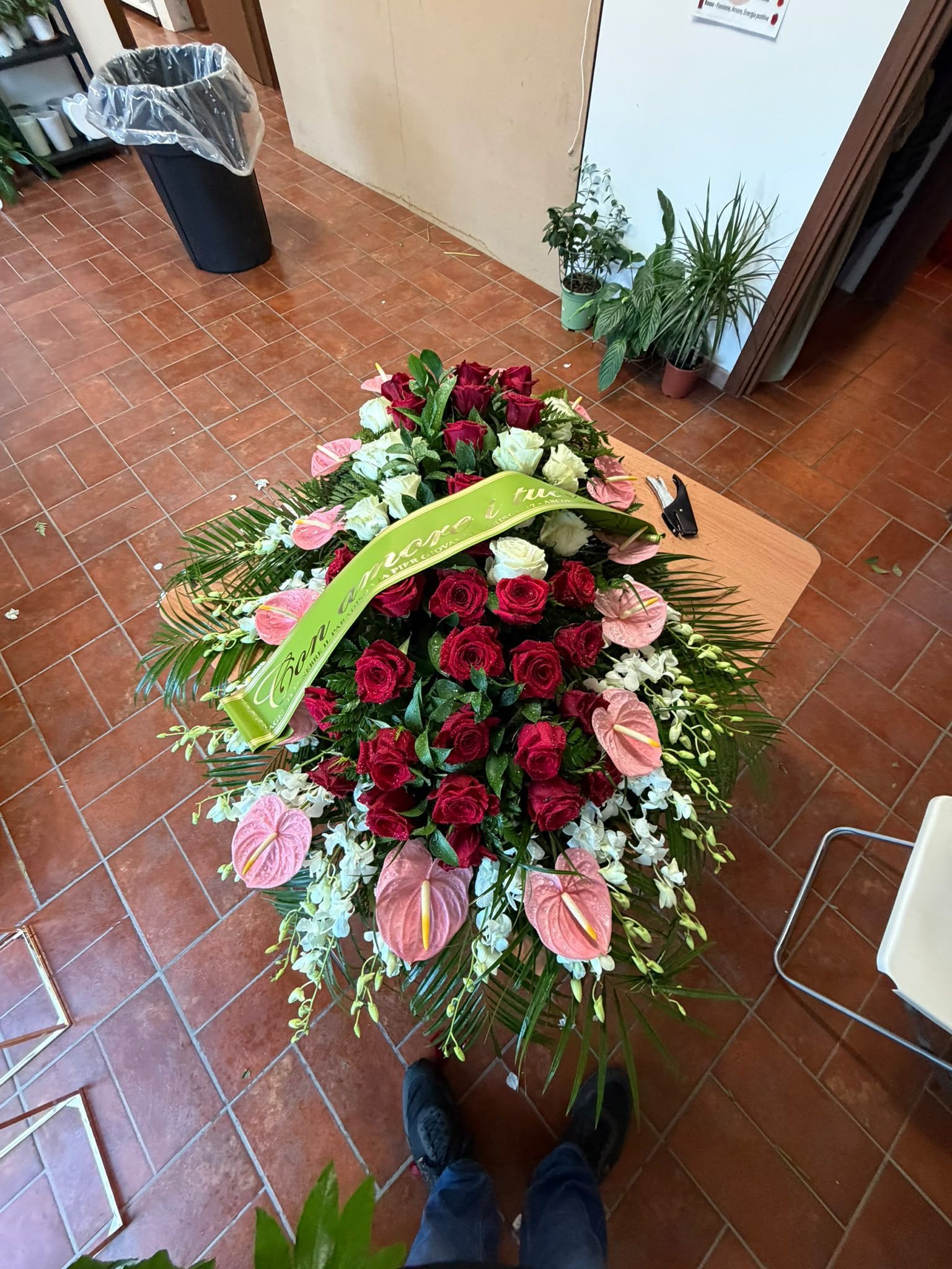 Grande bouquet di rose rosse con tocchi di rosa e nastro verde, su un pavimento piastrellato, visto dall’alto