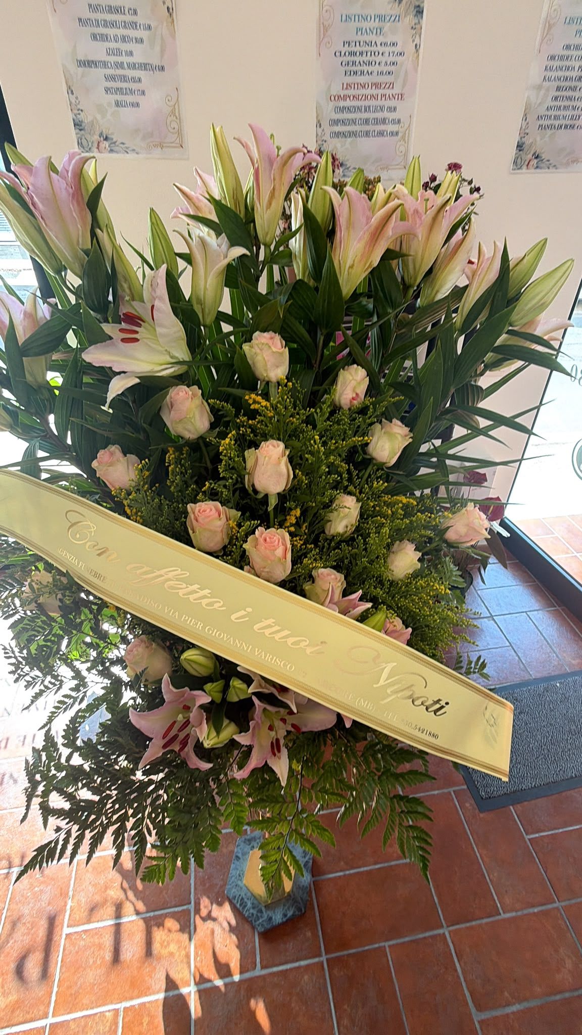 Grande composizione floreale funebre in rosa pastello e bianco, con nastro, esposta su un supporto all'interno