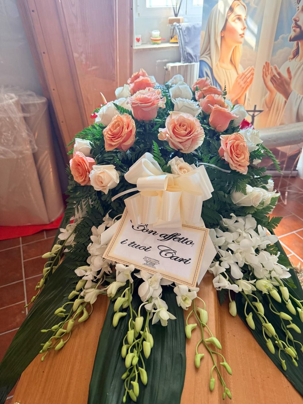 Una persona tiene in mano una rosa rossa accanto a candele accese e una foto incorniciata su un tavolo.