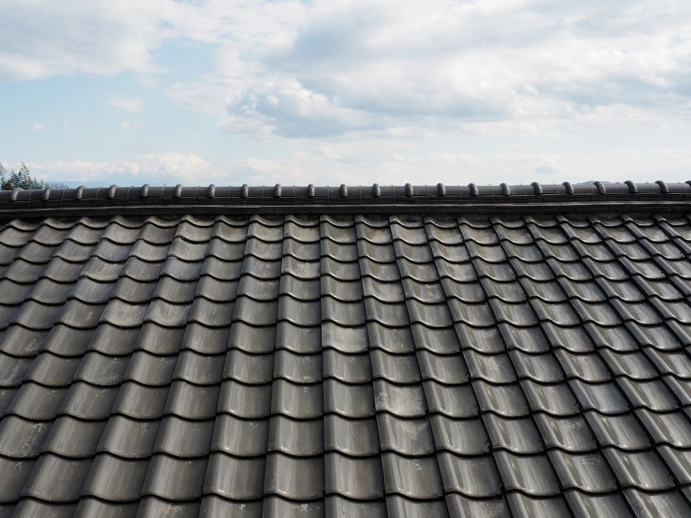Gray Tiled Roof Against a Cloudy Blue Sky — CP Roofing in Old Bar, NSW