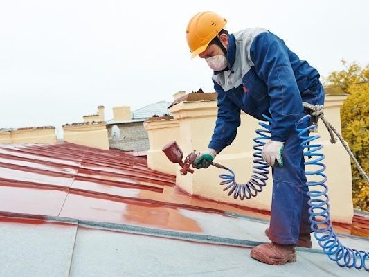 Man Wearing a Hard Hat and a Mask is Spraying Paint on a Roof — CP Roofing in Taree, NSW