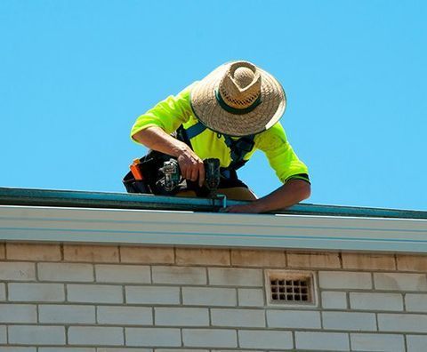 Man Wearing a Hat is Working on the Roof of a Building — CP Roofing in Wingham, NSW