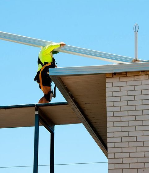 A Man Is Working On The Roof Of A Building — CP Roofing in Old Bar, NSW