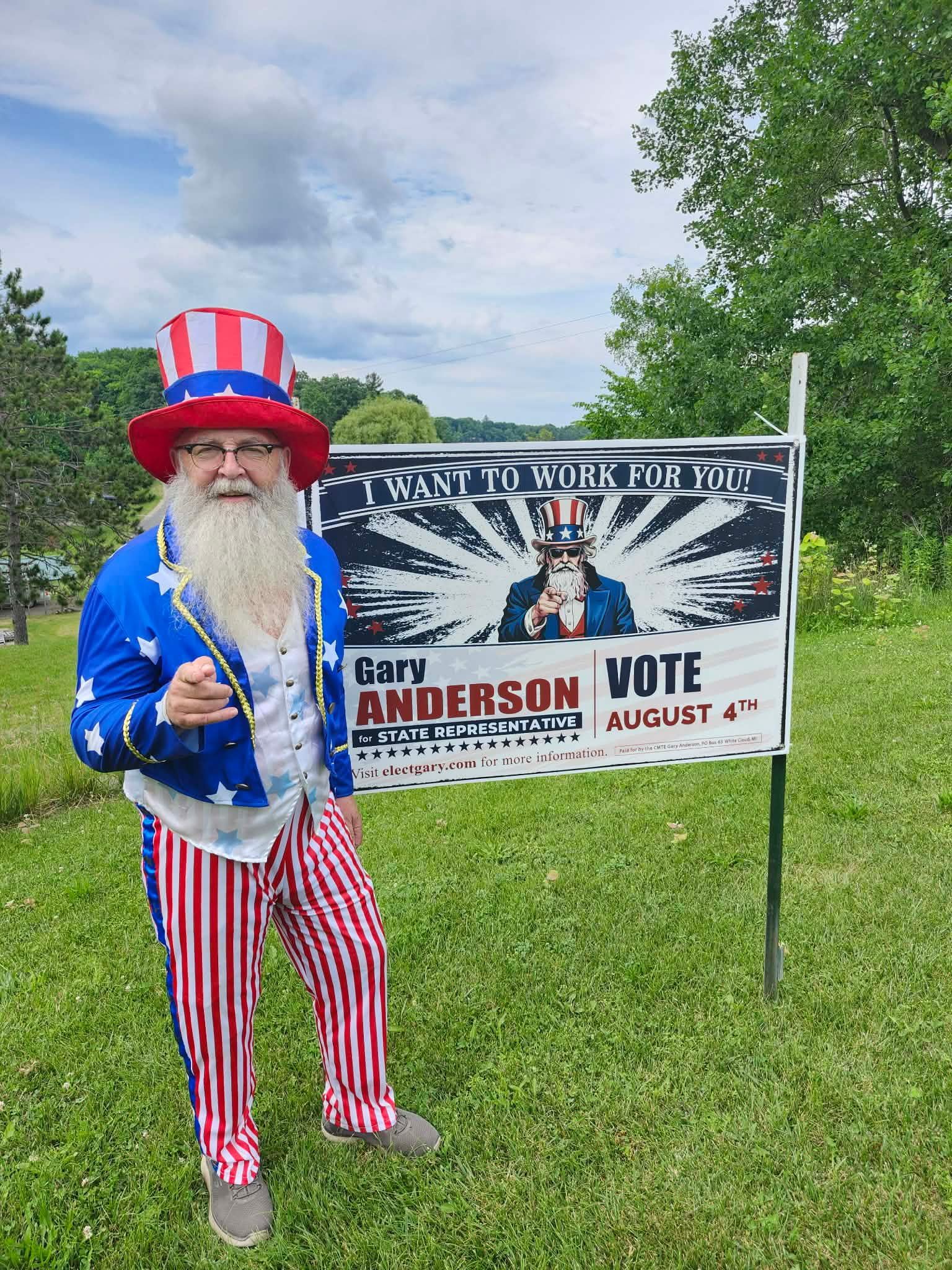 Garyin Uncle Sam outfit stands by Gary Anderson campaign sign in a grassy field.