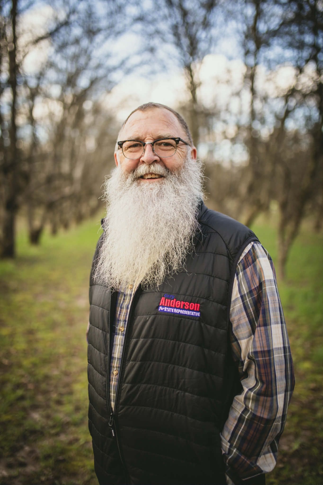 Man with long white beard holds American flag in snow.