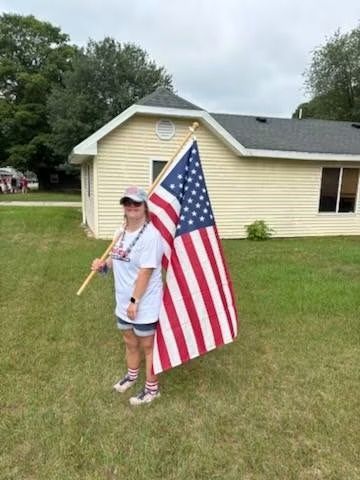 Child holding a large American flag on a grassy lawn in front of a house
