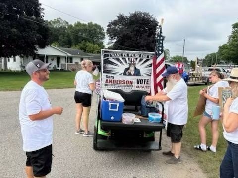 People gathered around a golf cart with a Barry Anderson Motel sign at an outdoor event