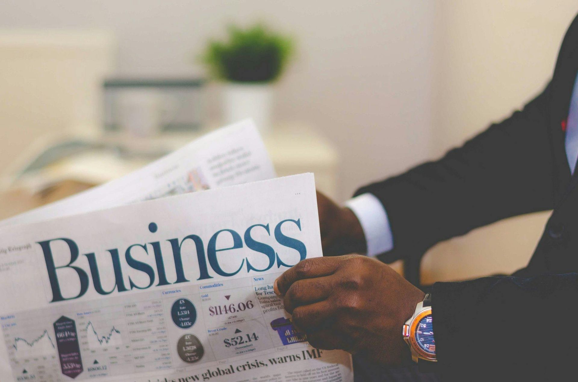 Person in suit reading a business newspaper with stock market data.
