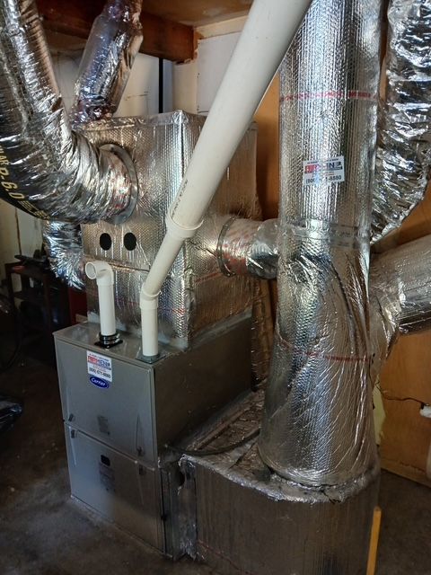 Basement HVAC furnace with insulated ductwork and white PVC pipes connected to metal units
