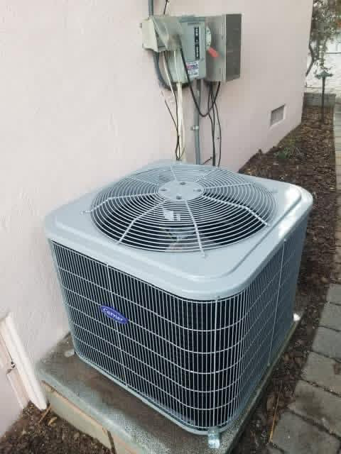 Outdoor air conditioner unit beside a wall with electrical box and hanging wires