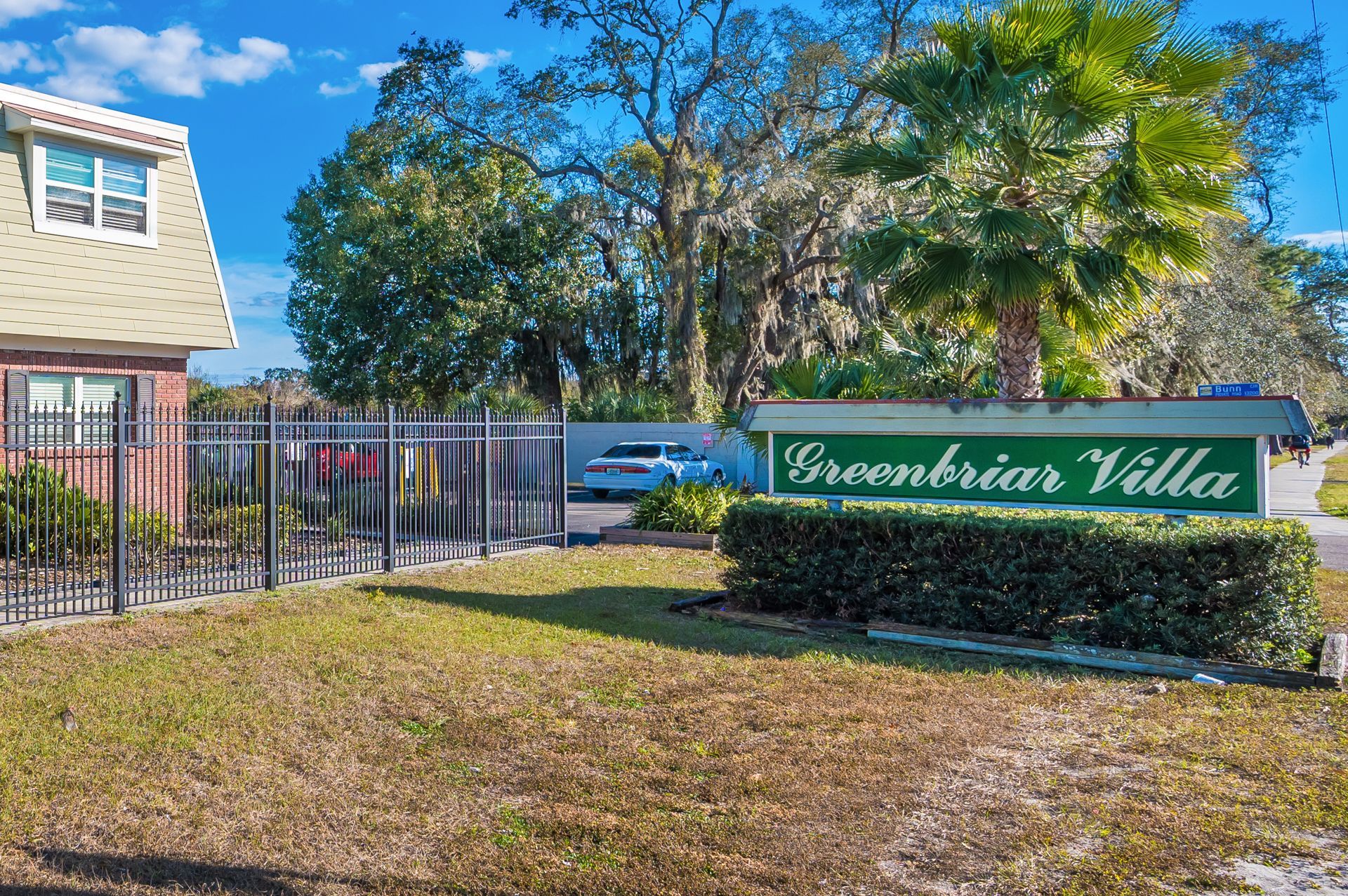 Sign for Greenbriar Villa with gate and building in background.