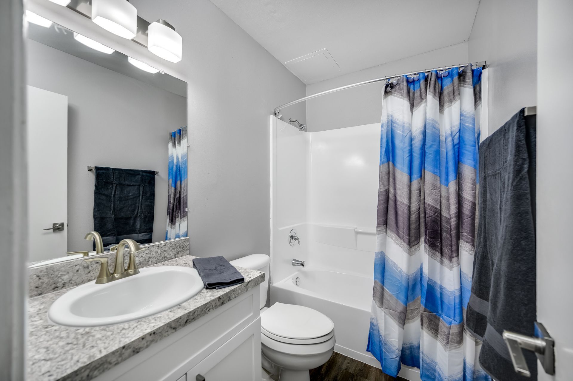 Bathroom with a gray vanity, white tub, and blue and gray striped shower curtain.