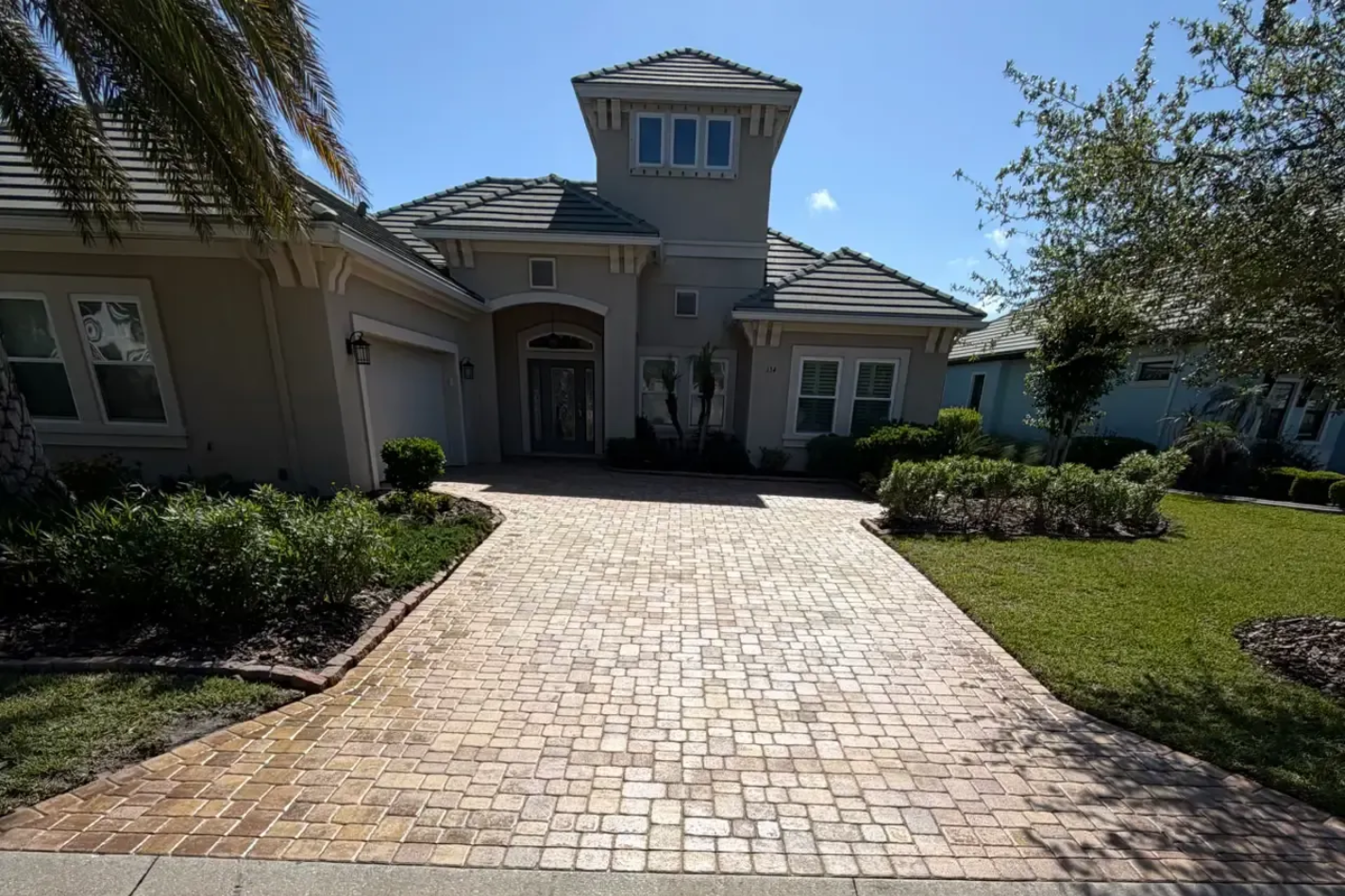 Sunlit brick driveway leading to a large house in Palm Harbor in Palm Coast, FL with a driveway of shiny, perfectly sealed pavers.