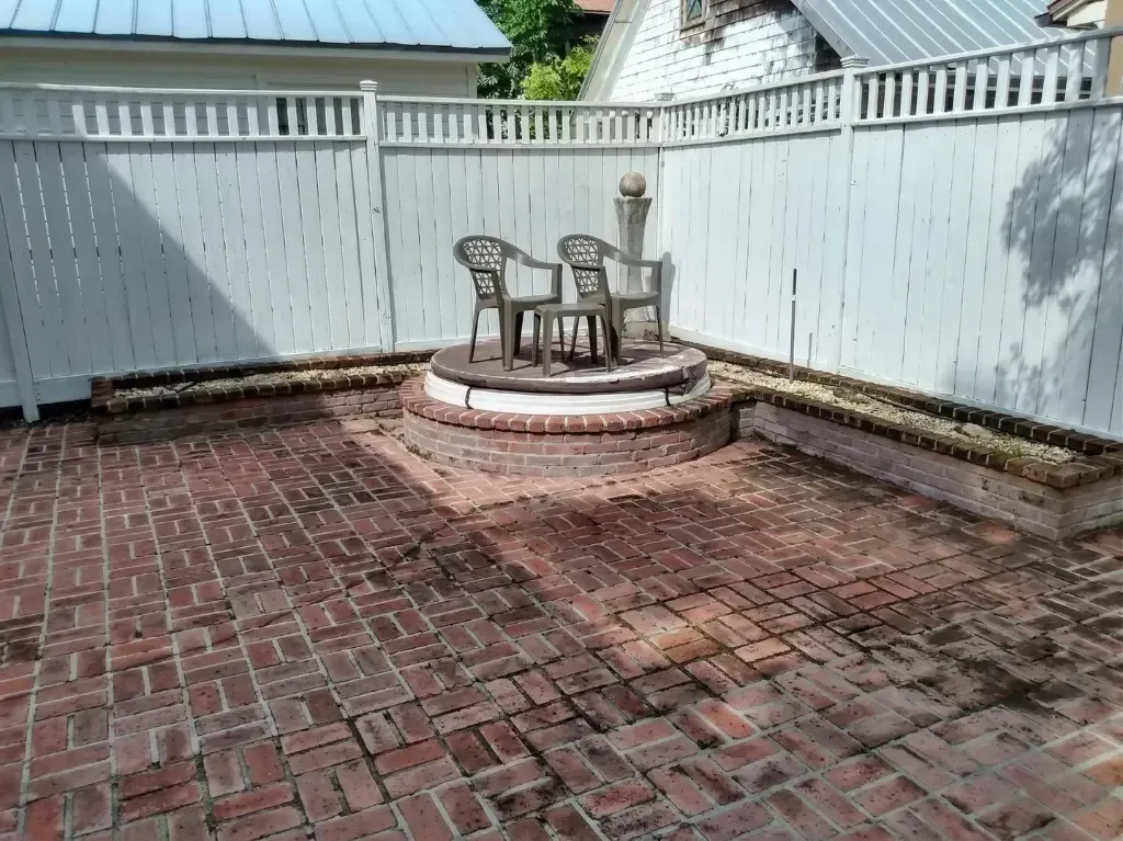Brick patio with a small round table and chairs on a raised circular platform beside a white fenced yard