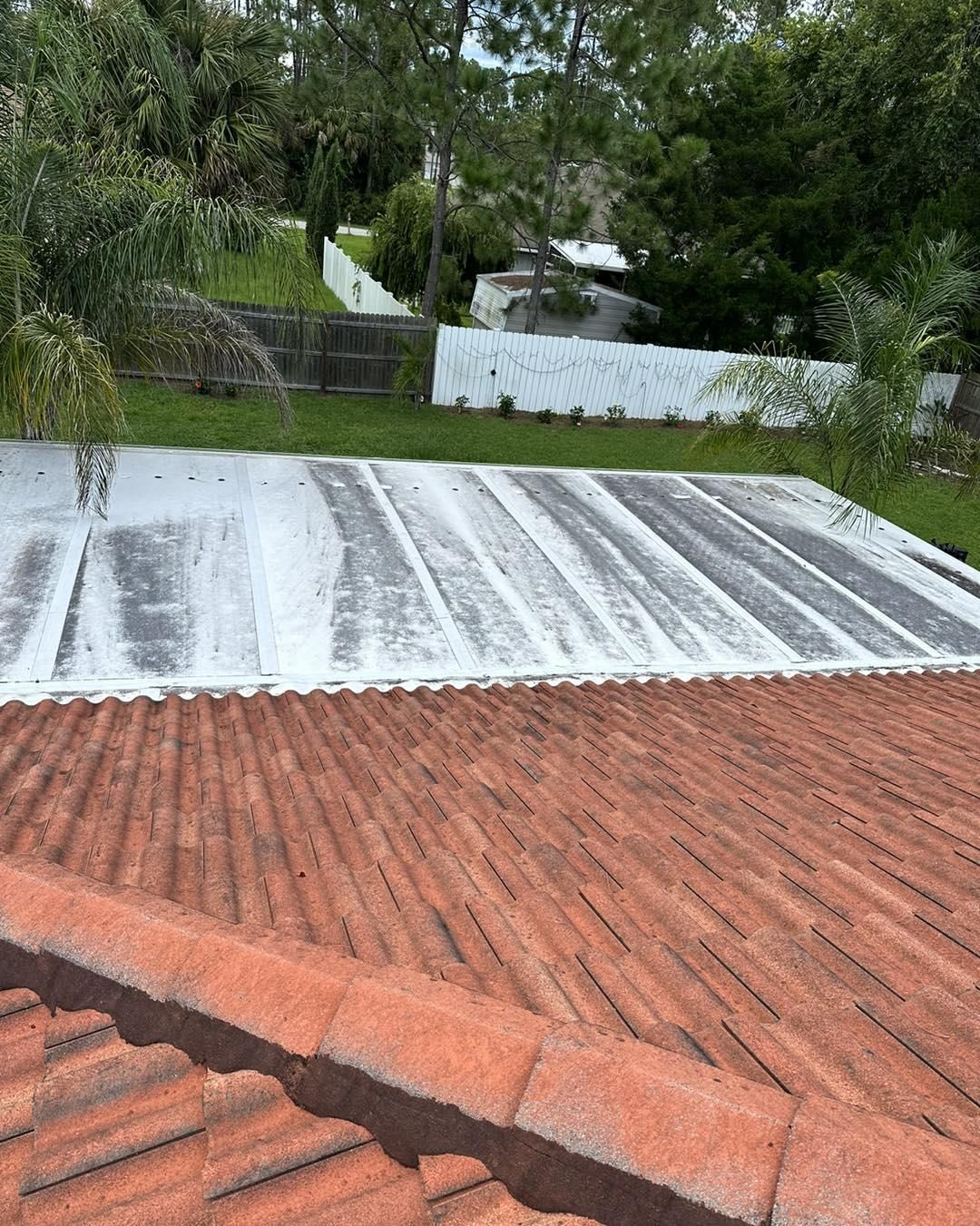 A high-angle shot shows a red tiled roof transitioning to a flat, white-coated roof section overlooking a backyard.