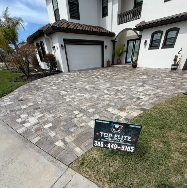 Flagler County's #1 House Wash Service A two-story white house with a paved driveway featuring a promotional sign for Top Elite Pavers.