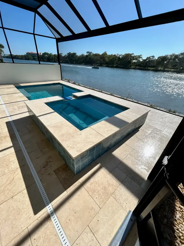 Covered patio with a rectangular pool and hot tub beside a calm waterfront view