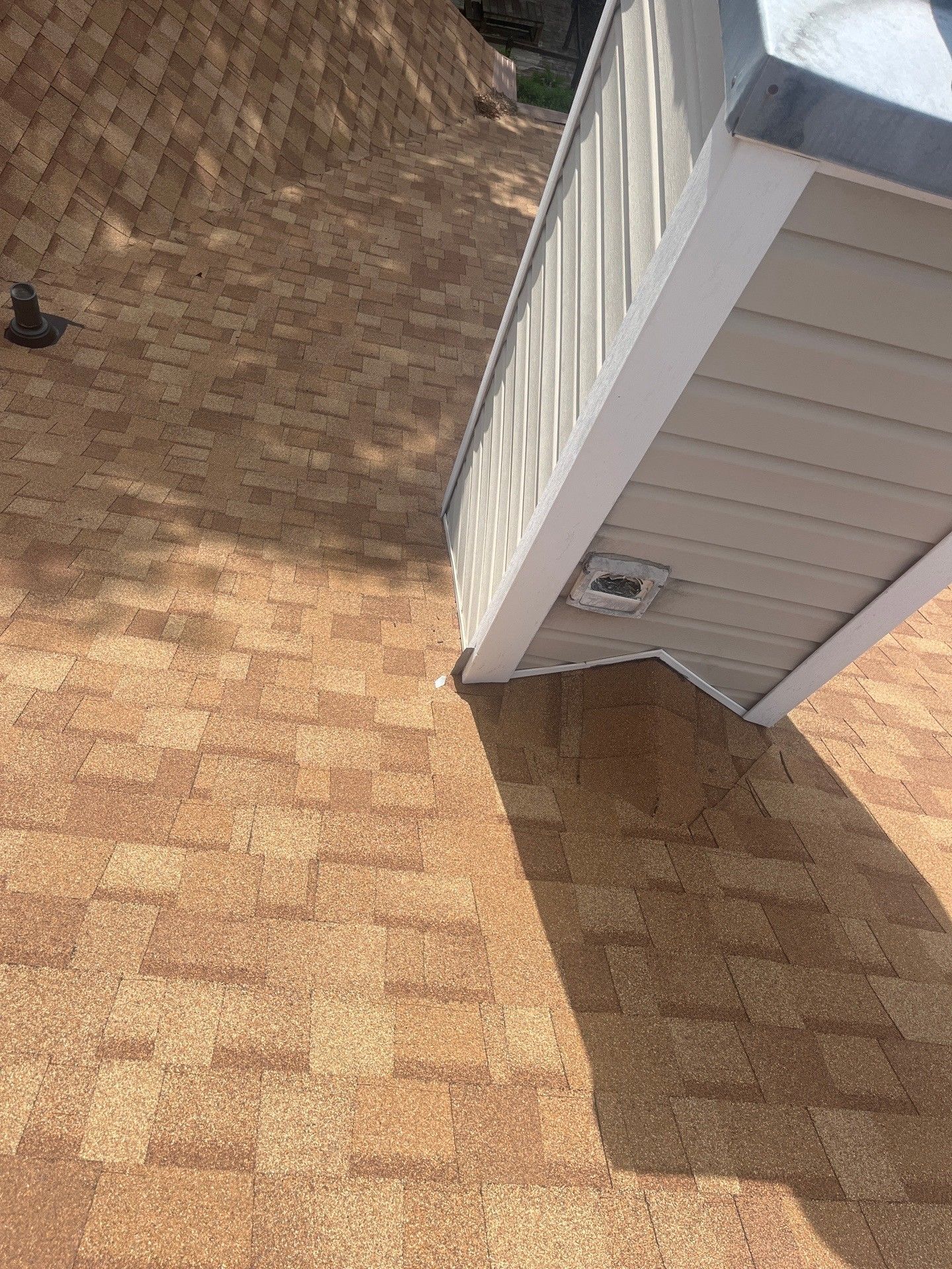 Tan shingle roof with a light-colored structure attached at an angle, casting a shadow.