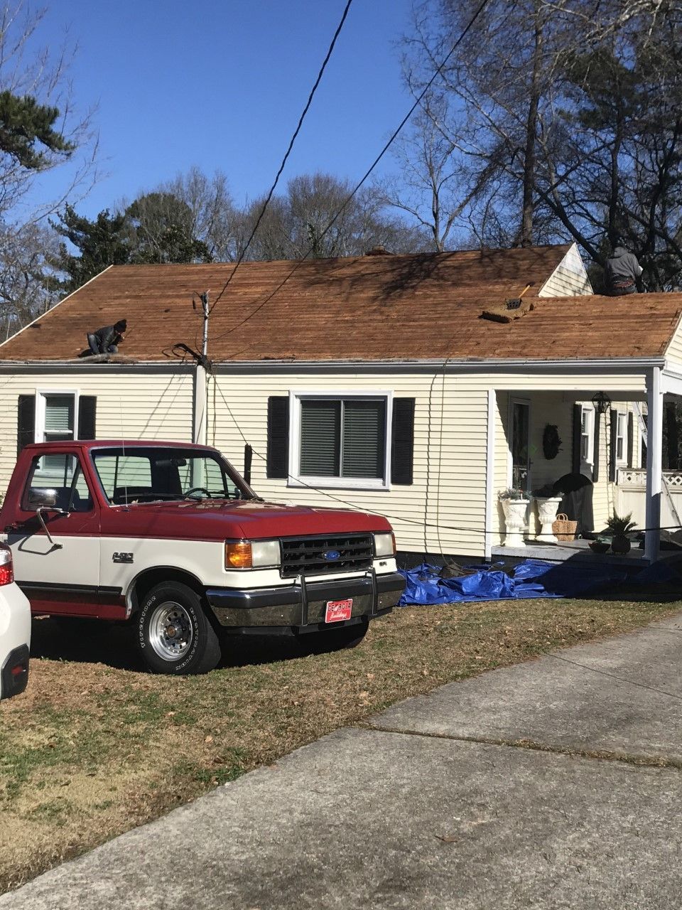 Red and white truck parked in front of a beige house with exposed roof, sunny day.