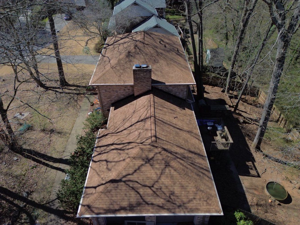 Aerial view of a brown roofed house with a brick chimney, surrounded by trees.