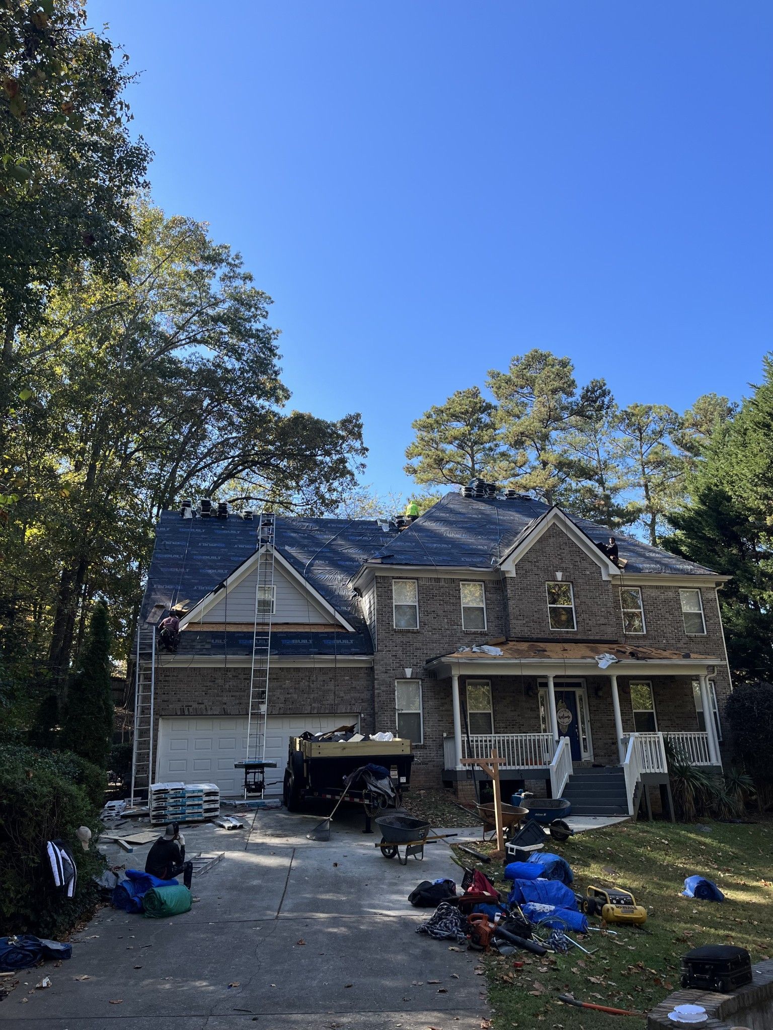 House under construction, roof and front porch dismantled, debris in driveway, sunny day.