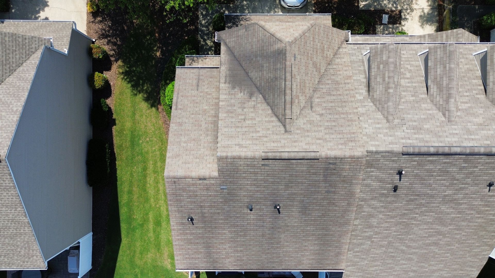 Overhead view of several buildings with gray shingled roofs and green grass between them.