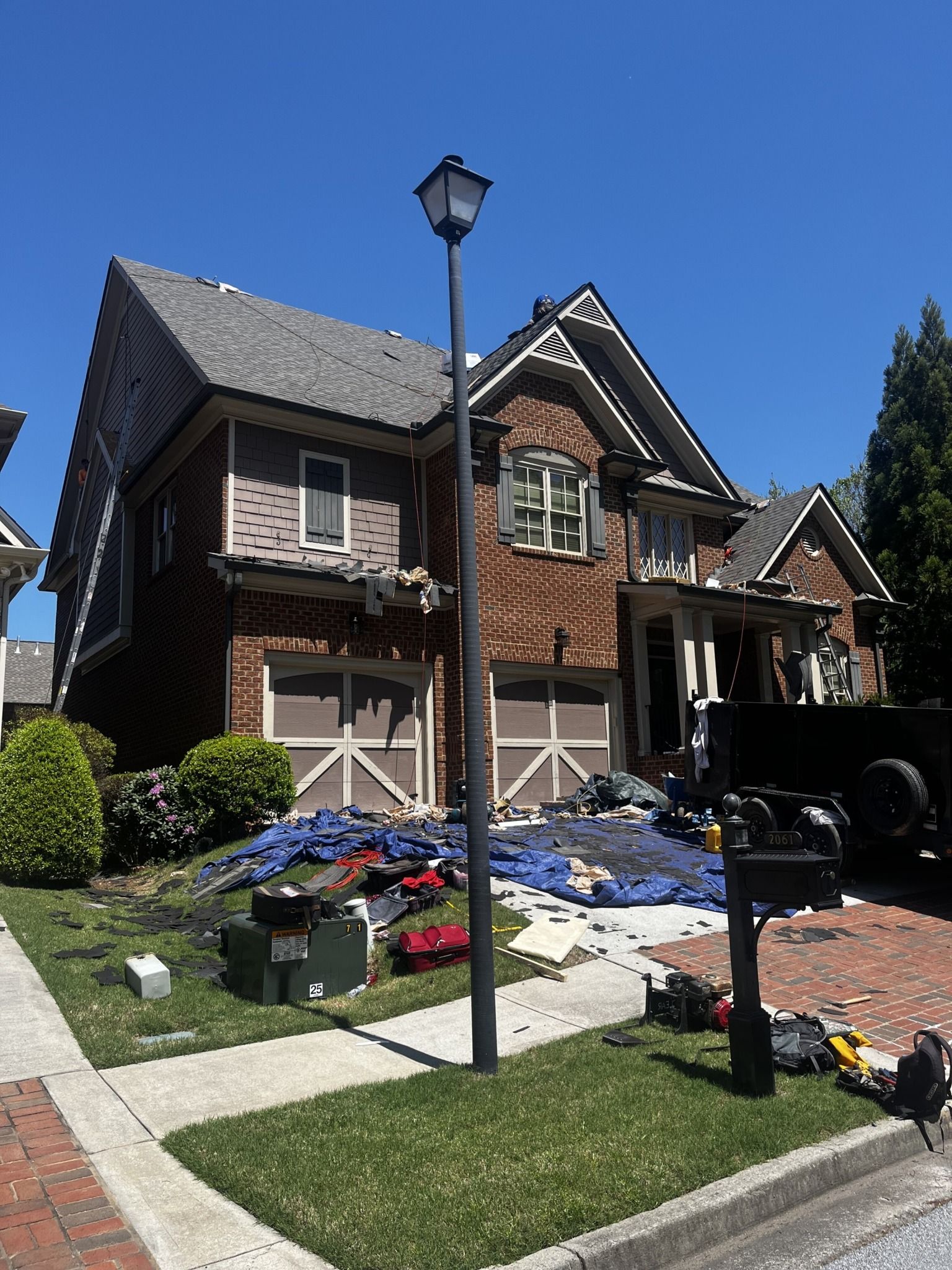 Two-story house with damaged roof, debris in driveway, and construction equipment.