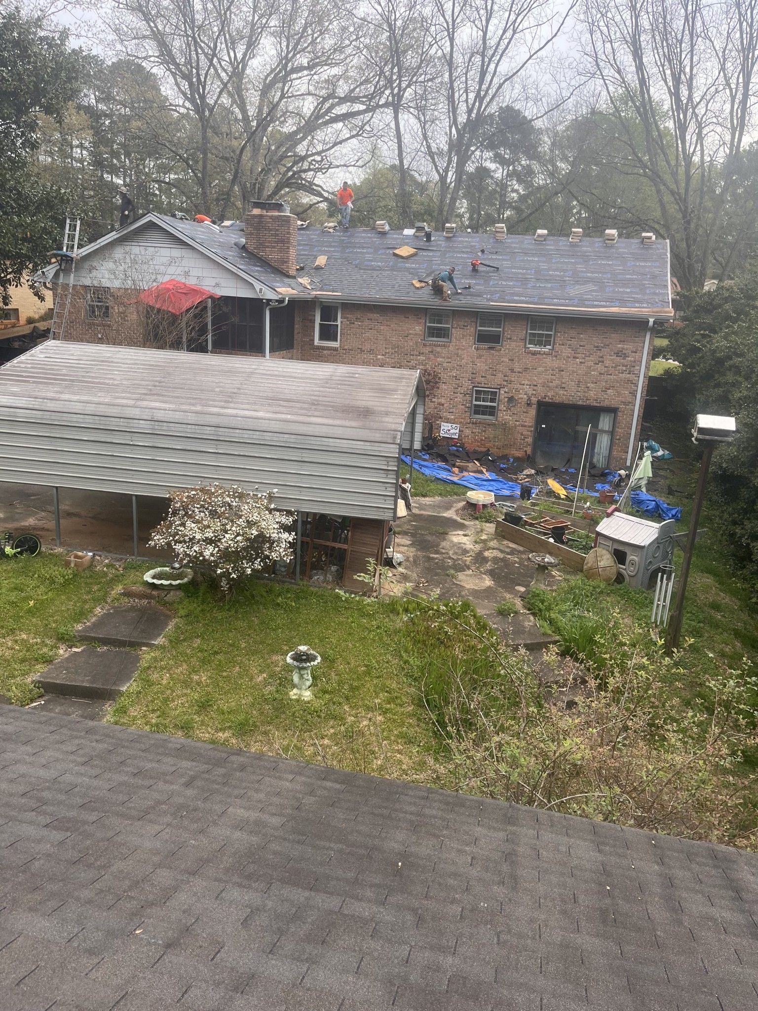 House with a brick exterior, a roof in progress, a patio area, and surrounding greenery.