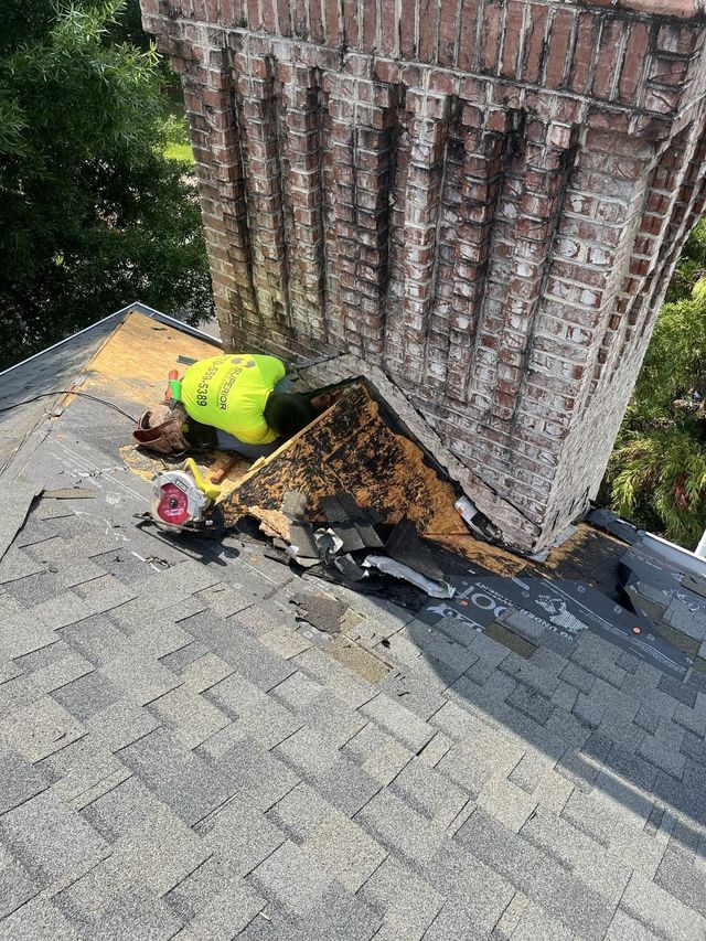 Chimney on roof with damaged flashing; debris and worker in yellow vest visible.