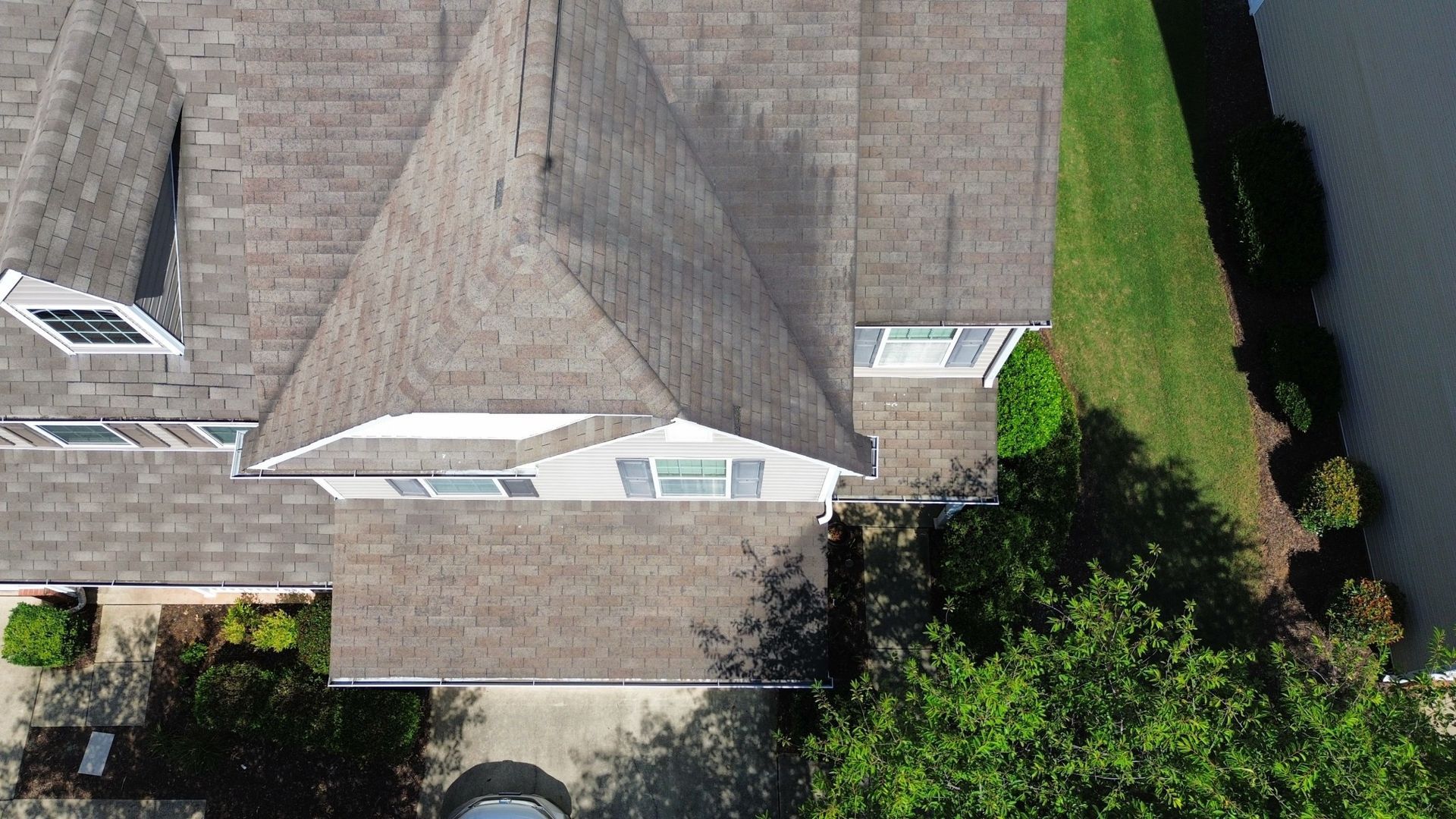 Overhead view of a house with a brown shingled roof, lawn, and water.