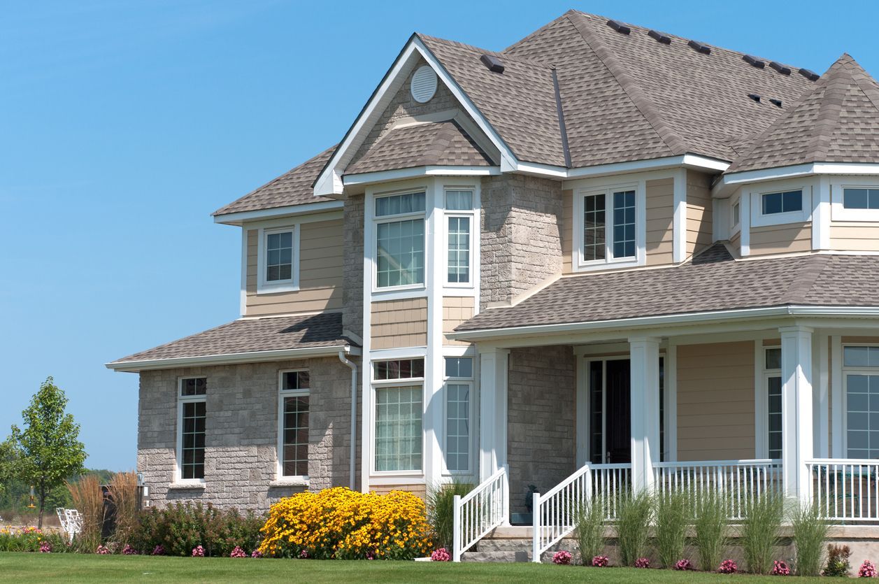 Two-story brick house with a porch and yard under a clear blue sky.