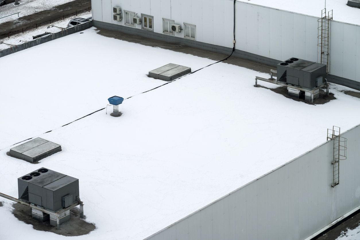 Snow-covered rooftop with ventilation units, access ladders, and a blue structure. White building exterior.
