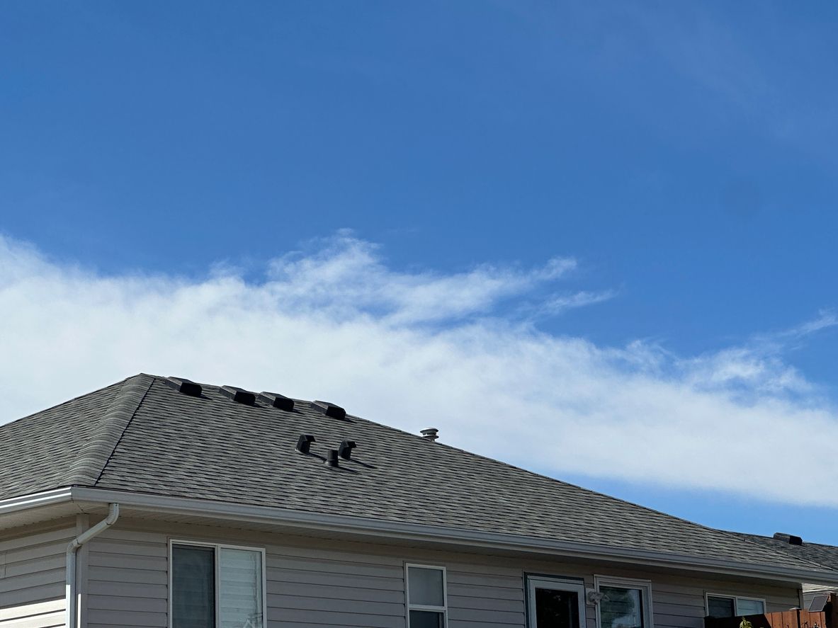 House roof with gray shingles against a blue sky with scattered clouds.