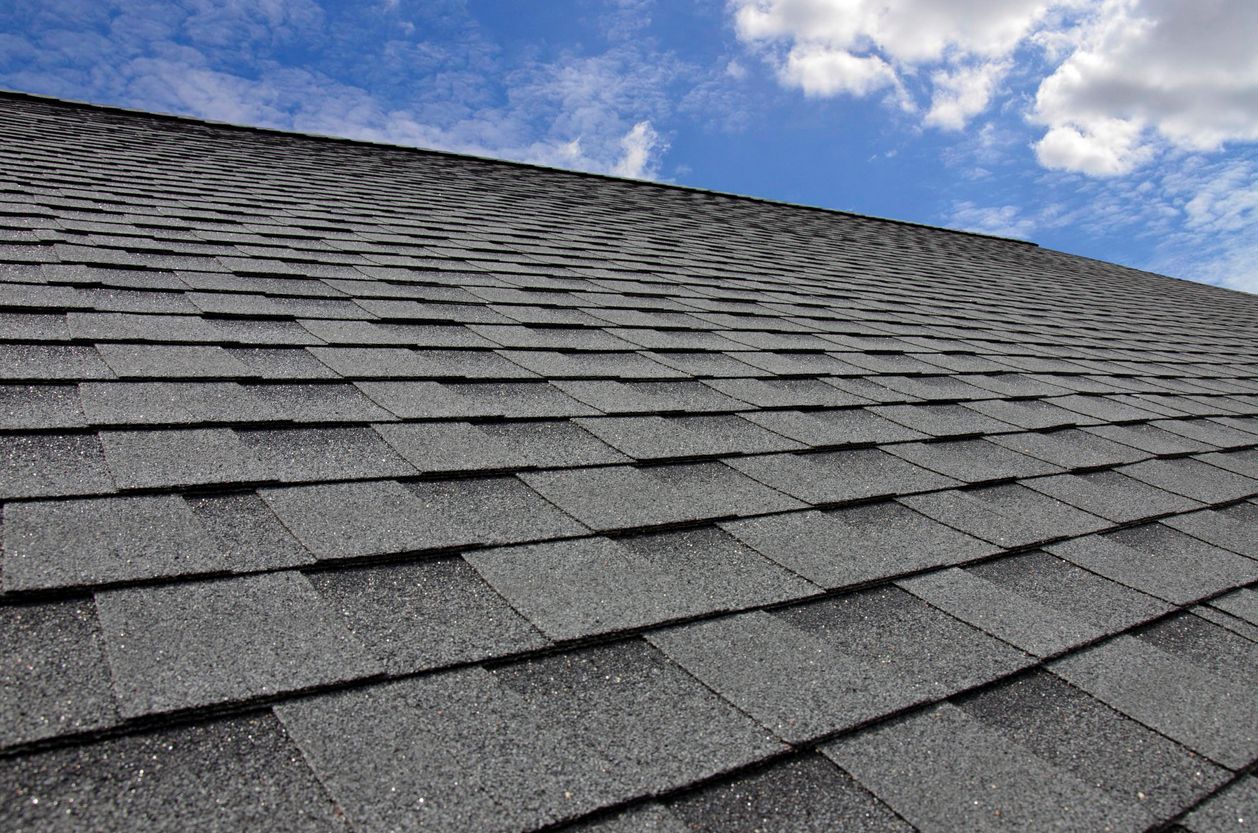 Gray asphalt shingle roof against a blue sky with white clouds.