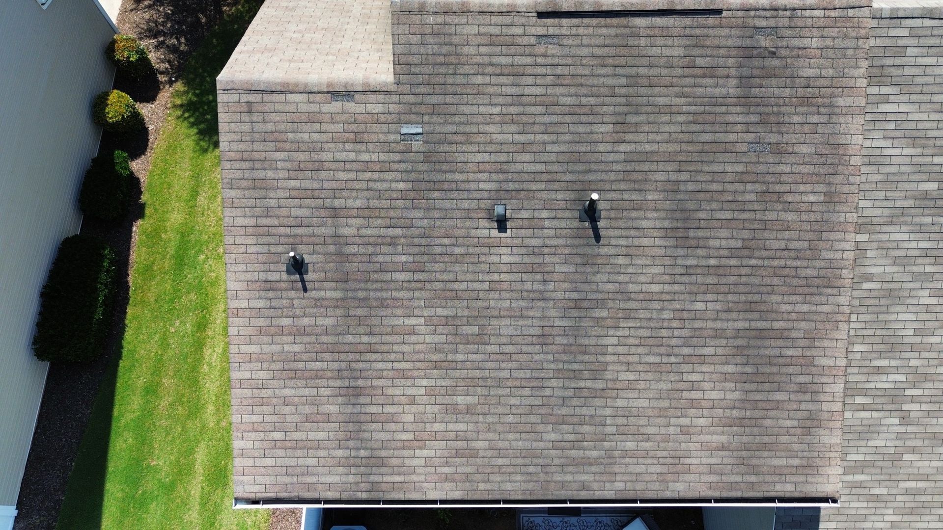 Overhead view of a house roof with several vents and some greenery along the side.