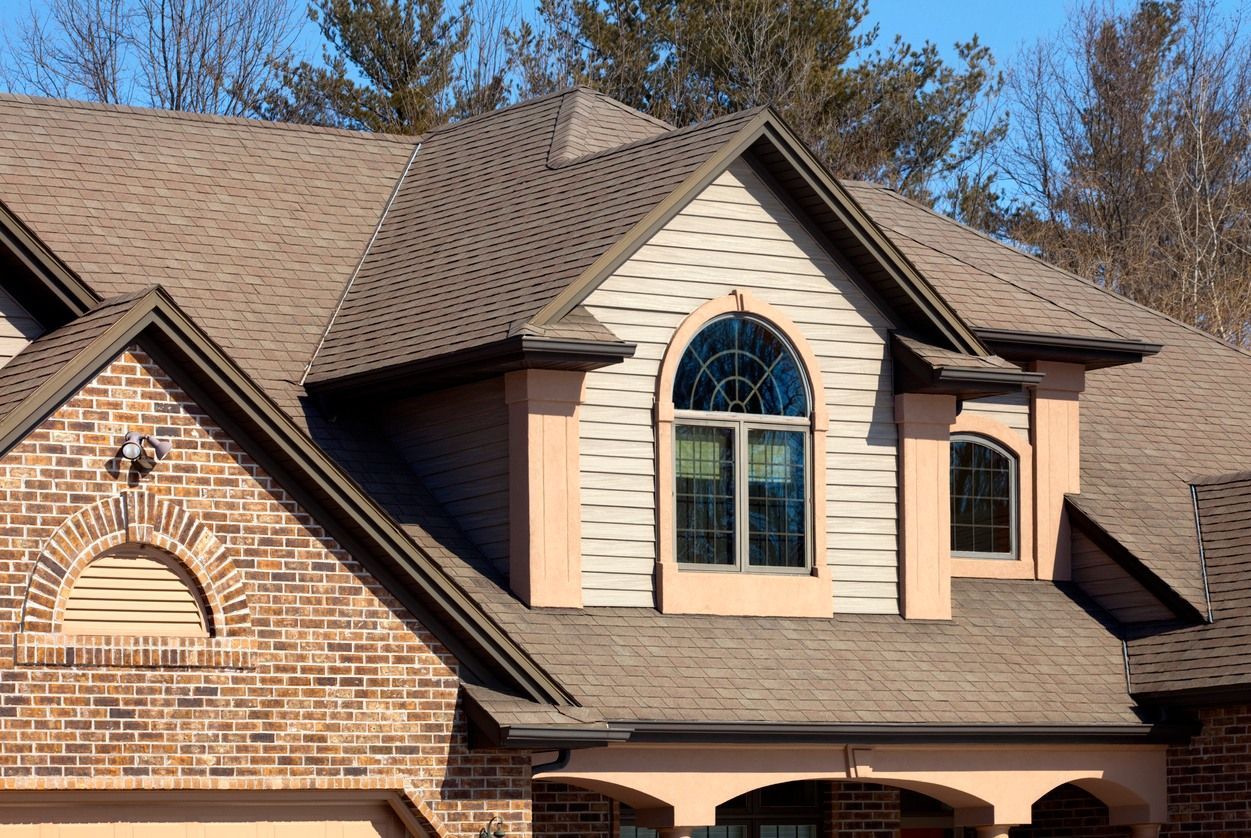 House with brown roof and brick and tan siding, arched window.