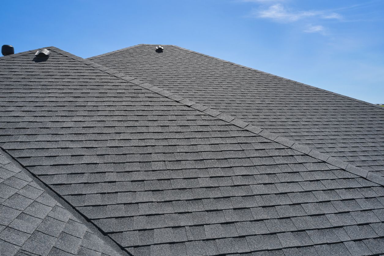 Close-up of a gray shingled roof under a blue sky, vents visible.