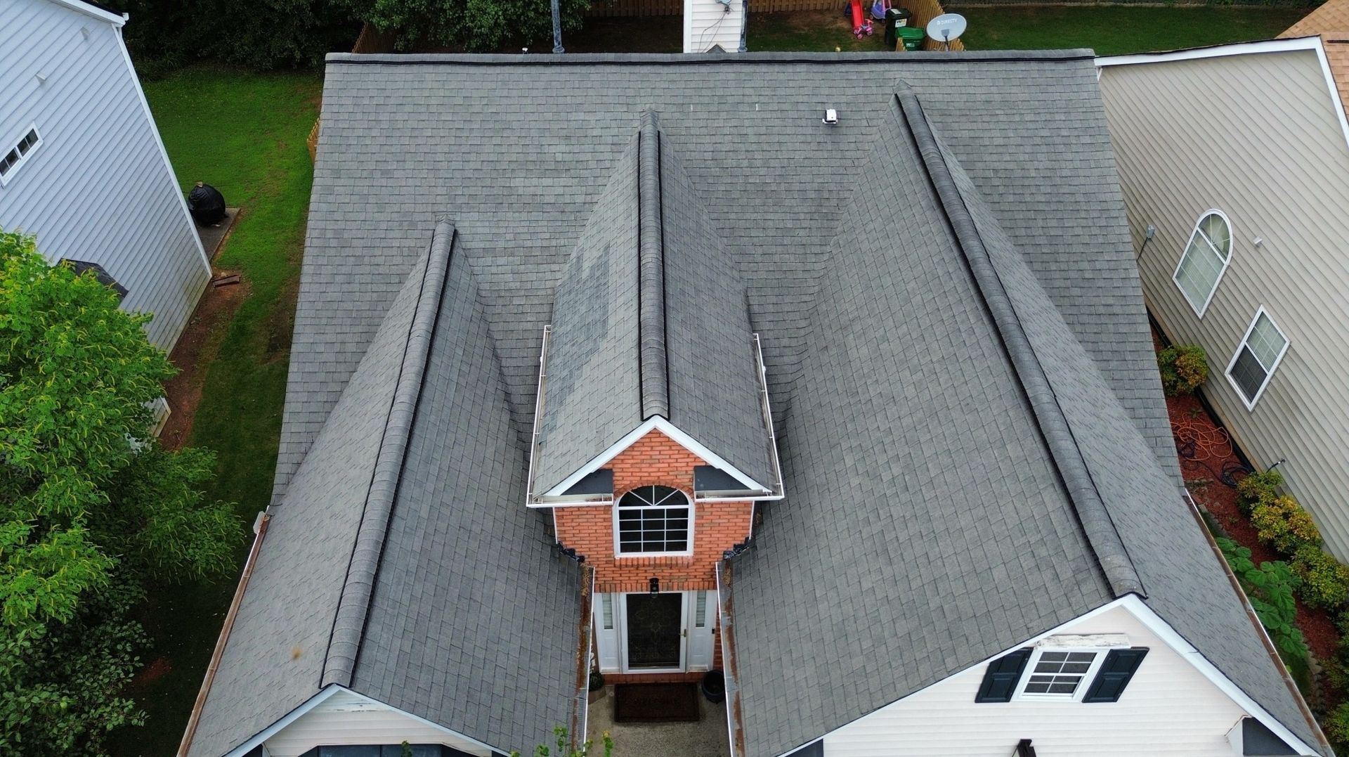 Aerial view of a house with a grey roof. A red-orange gable and dark shutters are visible.