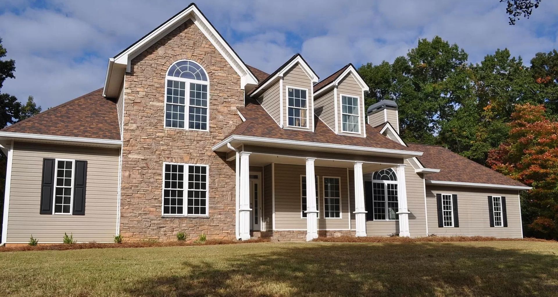 Two-story house with brick and siding exterior, front porch, and landscaped lawn on a sunny day.