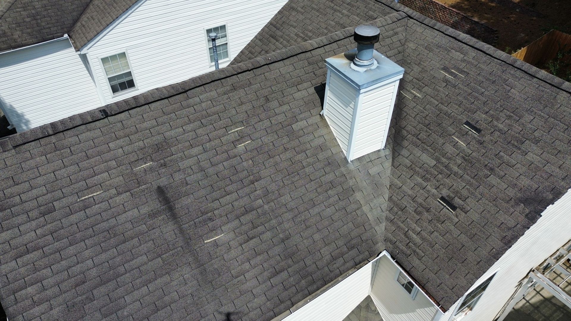Overhead view of a dark gray asphalt shingle roof with a white chimney.