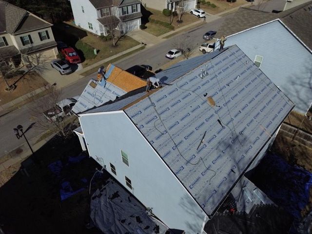 Aerial view of a house with damaged roof and construction materials in a residential neighborhood.