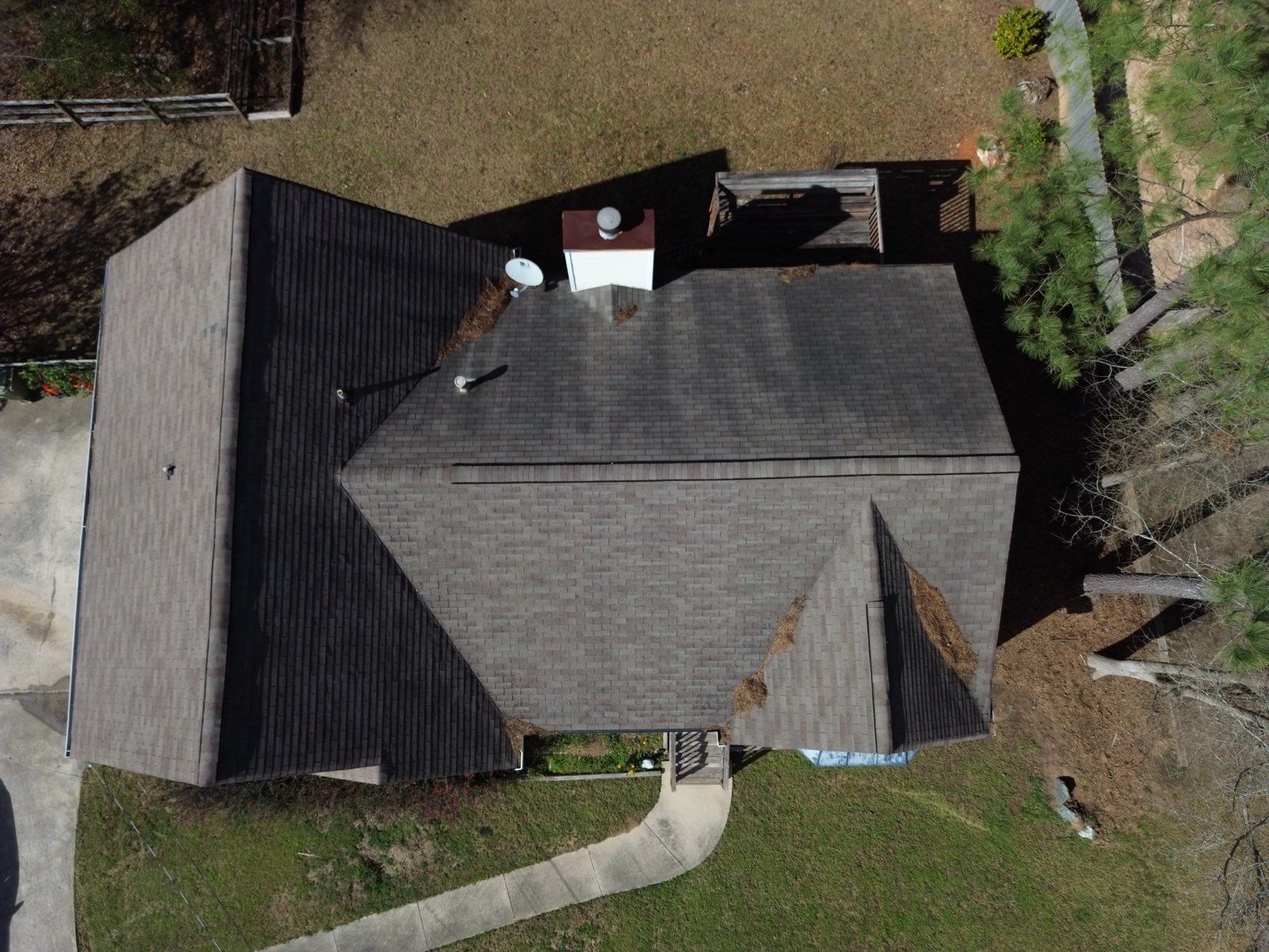 Overhead view of a house with a brown roof, chimney, and satellite dish; surrounded by grass and trees.