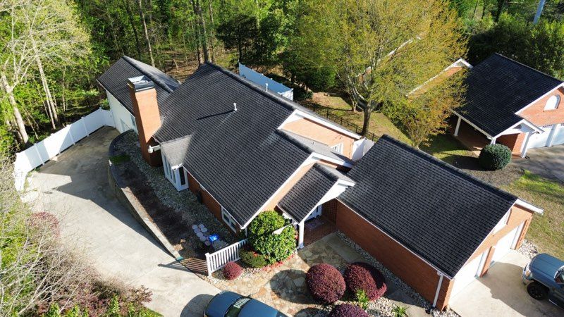 Aerial view of a red brick house with a black roof, surrounded by trees and a white fence.