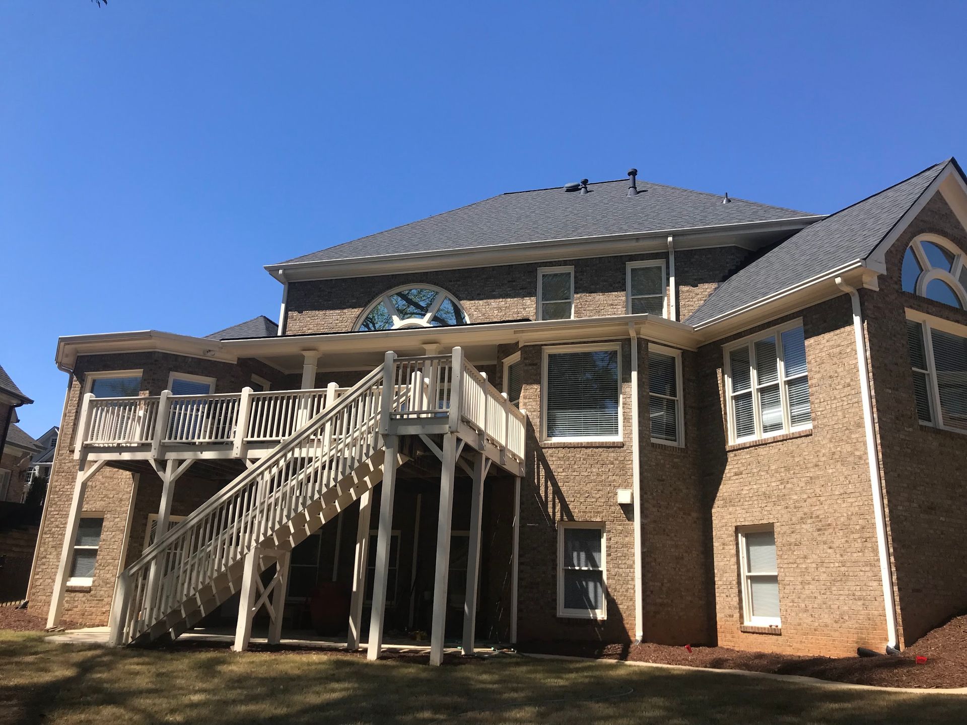 Brick house with a wooden deck and staircase under a clear blue sky.